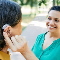 Woman with hearing aid chats with her friend outside.